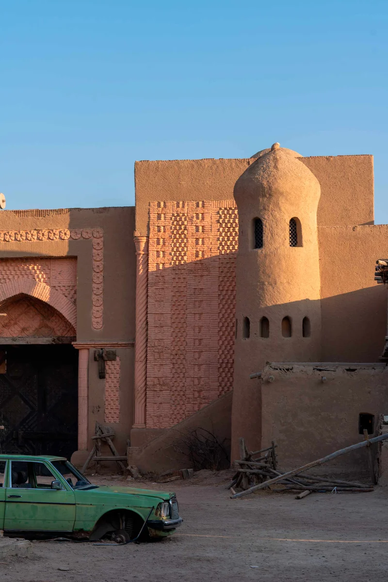 Old green car parked beside mud-brick fortress walls of a movie set